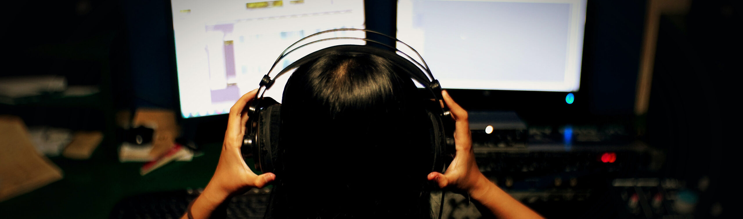 Woman wearing headphones looking at two computer screens
